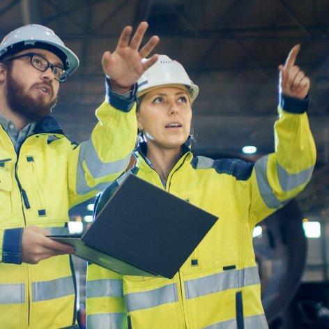 Ein Mann und eine Frau die einen Bauhelm und eine Warnjacke tragen 