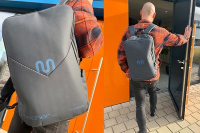 Der Träger des Rucksacks, gekleidet in ein kariertes Hemd, geht durch eine Glastür in einem urbanen Umfeld.